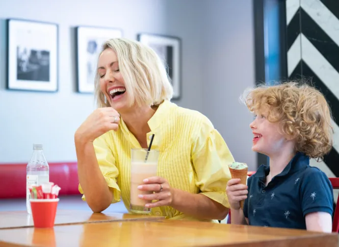 A mum and young son sitting down and laughing together at Cibo Espresso in Prospect. The mum is holding a smoothie glass and the son is eating an ice cream cone.