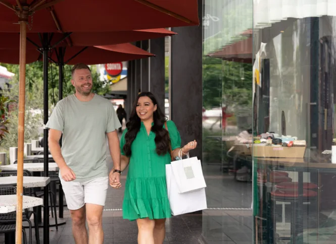 Man and woman holding hands walking down Prospect Road. Woman is holding shopping bags.